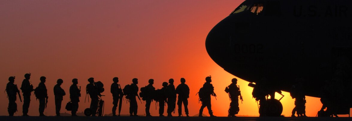 Soldiers bording an airplane against a sunset.